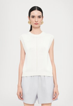 Top senza maniche in maglia bianca con scollatura tonda, caratterizzato da un dettaglio a linea centrale. Abbinato a pantaloni corti di colore grigio chiaro, in tessuto leggero e ampio.
