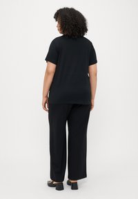 Μαύρη κοντομάνικη μπλούζα συνδυασμένη με χαλαρές μαύρες παντελόνες, με άνετη εφαρμογή και λεία υφή, φορεμένες με παπούτσια με τετράγωνο τακούνι.