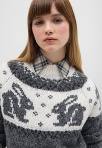 Gestrickter Pullover mit grauem und weißem Farbschema, mit Kaninchenmotiven auf der Brust, einem strukturierten Muster und einem Rundhalsausschnitt.
