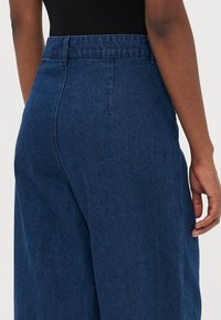 Dark blue high-waisted denim trousers with a smooth texture, wide leg design, and clean back seam detail.