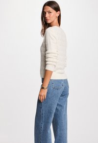 Maglione color crema, texturizzato, con un motivo a onda e polsini a coste, abbinato a jeans in denim azzurro a vita alta.