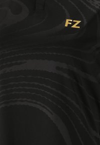 Svart polotröja med ett subtilt vågmönster, tillverkad av mjukt tyg, med en gyllene "FZ"-logotyp på vänster bröstområde.