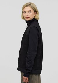 Schwarze Zip-Up-Jacke mit einem Fleece-Vorderteil und glatten Ärmeln, hohem Kragen und seitlichen Reißverschlusstaschen, entworfen für Wärme und Komfort.