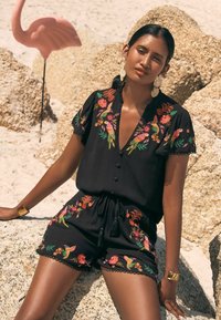 Black embroidered romper featuring colorful floral and bird patterns, short sleeves, V-neckline, and a drawstring waist.