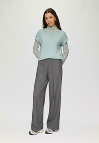 Lichtblauwe korte mouw top, gelaagd over een grijze lange mouw shirt, gecombineerd met grijze wijde broek en zilveren sportschoenen. Eenvoudig ontwerp.