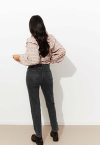 Chemisier à carreaux rose clair avec des manches froncées, associé à un jean taille haute gris foncé et des bottes chunky marron. Fond minimaliste.