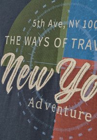 Koszulka z grafiką, która łączy niebieskie, zielone i czerwone sekcje, z haftowanym napisem "Nowojorska Przygodowa" oraz elementami projektu kompasu.