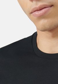 Schwarzes Baumwoll-T-Shirt mit Rundhalsausschnitt, glatter Textur und normaler Passform, mit Nahaufnahme des Ausschnitts und der unteren Gesichtshälfte.