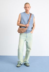 Bolso bandolera marrón claro con un acabado texturizado, top sin mangas azul, jeans de mezclilla azul claro descoloridos y zapatillas verdes con acentos estampados.
