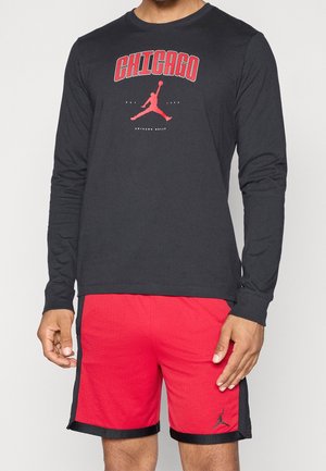 Homme portant un t-shirt noir à manches longues avec le logo rouge des Chicago Bulls et un short de basket rouge avec des bordures noires et le logo Jumpman.