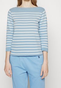 Haut à manches longues bleu clair avec des rayures blanches horizontales, encolure bateau et tissu doux. Associé à un pantalon de survêtement bleu assorti.