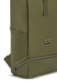 Olivově zelený batoh vyrobený z texturované tkaniny, obdélcového tvaru, s zipem na spodní části a malou značkovou etiketou na boku.