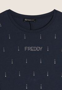 Camiseta de manga corta en azul marino hecha de una tela suave, con detalles de cristal en líneas verticales, y el texto "FREDDY" en lentejuelas en la parte delantera.