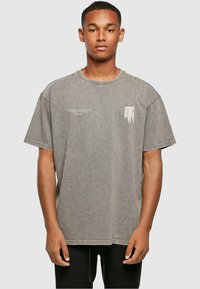 Grå oversized t-shirt lavet af blød bomuld med rund halsudskæring. Har minimale hvide logo-accenter og en slidt tekstur.