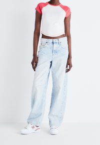 Avskuren vit topp med korallfärgade ärmar, ihop med ljusblå vida jeans. Vita sneakers med röda och orange detaljer fulländar looken.