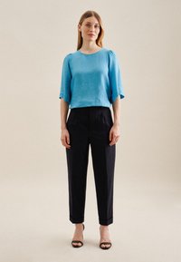 Blusa in lino azzurro chiaro a maniche corte abbinata a pantaloni neri su misura e sandali con tacco neri. Design semplice e pulito con risvolti.