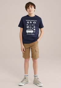 Marine katoenen T-shirt met witte zomerse graphics, gecombineerd met tan cargoshorts en hoge grijze sneakers met zwarte en witte accenten.