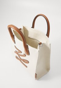 Canvas tote taske i off-white med brune læderhåndtag, med et broderet design foran og en lynlåslomme indeni.