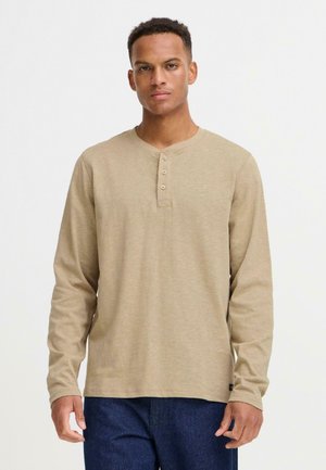 Chemise henley à manches longues beige en tissu doux, présentant un col rond, une patte de boutonnage à trois boutons et un léger motif texturé.