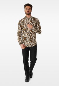 Srajca s leopardjim potiskom v bež barvi s črnimi in oranžnimi pikami, z gumbi na sprednji strani, dolgimi rokavi, kombinirana s črnimi hlačami in čevlji.