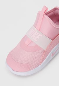 Baskets rose clair avec une tige en mesh, sangle extensible arborant le logo "NIKE", col rembourré et semelle en caoutchouc blanc avec un design subtil.