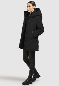 Must mustriga musta pikem puhv mantli kapuutsiga, millel on esine zipp, küljetaskud ja voolujooneline siluett. Kandub mustade retuuside ja saapade peale.