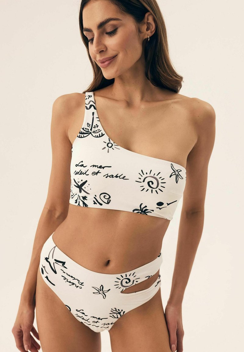 Bikini top na jedno ramię i wysoki dół w kolorze białym z czarnymi nadrukami graficznymi, z wycięciami wzdłuż pasa.