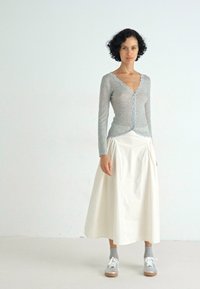 Lichtgrijs longsleeve shirt met gegolfde randen, gedragen met een witte midi rok. Gecombineerd met grijze sneakers en enkelkousen. Eenvoudig ontwerp.