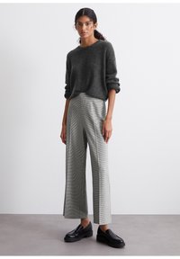 Grijze gebreide trui met opgerolde mouwen, gecombineerd met hoge taille, wijd uitlopende houndstooth broek en zwarte platformloafers.