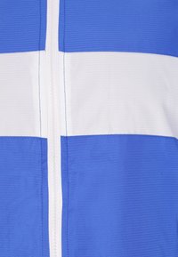 Jachetă bleu și albă cu fermoar, având dungi orizontale, material texturat și cusături contrastante pe lângă fermoar.