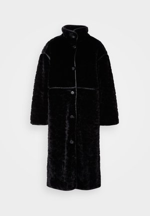 Abrigo de borreguillo negro con un alto cuello, con un cierre frontal de botones, corte holgado y superficie texturizada. La parte superior tiene costuras contrastantes.