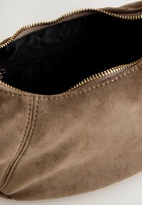 Borsa in suede marrone con interno nero, dotata di una cerniera dorata e dettagli di cucitura visibili. Si apre ampiamente per un facile accesso.