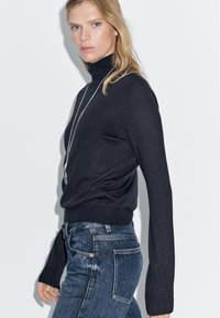 Navy turtleneck sweater in soft material with long sleeves and ribbed hem, paired with blue denim jeans featuring back pockets.