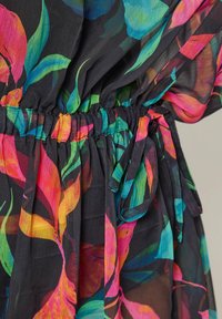 Gros plan sur une robe en tissu noir transparent avec un imprimé floral abstrait vif en rose, orange, bleu et vert, taille élastique froncée avec ceinture à nouer.
