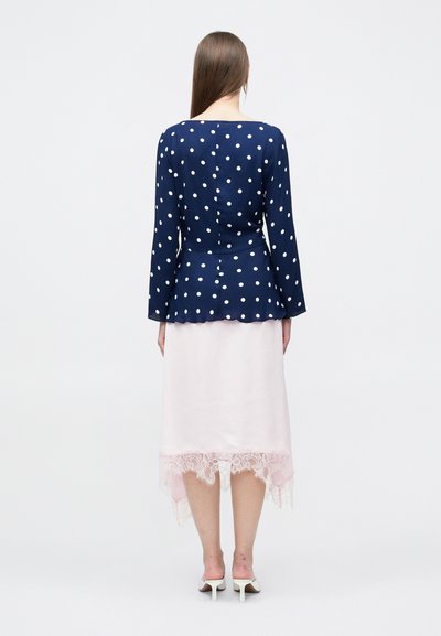 Μπλε ναυτικό τοπ με πουά, μακριά μανίκια και σχέδιο πεπλούμ, σε συνδυασμό με ροζ φούστα με δαντέλα στο τελείωμα. Ορατά τα τακούνια.