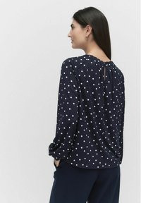 Navyblauwe blouse met lange mouwen en witte stippen. Heeft een geplooide halslijn en een sleutelgatendetail aan de achterkant, gemaakt van een soepele stof.