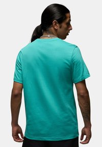 T-shirt corta turchese realizzata in cotone liscio, con colletto tondo e vestibilità regolare, vista da dietro, senza dettagli particolari.