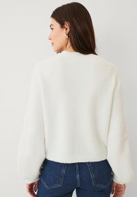 Witte, fluffy trui met een ronde halslijn en lange, gepofte mouwen. Verkorte uitvoering met een geribbelde zoom, gecombineerd met strakke blauwe jeans.