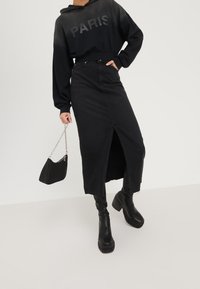 Sudadera corta negra con el texto "PARIS", combinada con una falda de mezclilla negra con una abertura frontal. Los accesorios incluyen un bolso negro y botas gruesas.