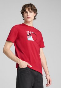 Camiseta de algodón roja con un diseño gráfico que presenta formas geométricas en azul, rosa y negro. Manga corta y escote redondo.