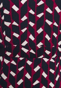 Sukienka z tkaniny o geometrycznym wzorze w kolorach bordowym, granatowym i białym. Materiał ma fakturowane wykończenie, a sukienka jest dopasowana w talii.