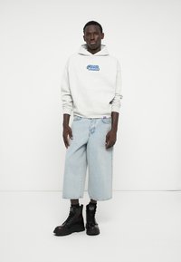 Sudadera gris claro con gráfico azul, culottes de mezclilla clara de gran tamaño, y botas negras con cordones de acabado texturizado y suelas gruesas.