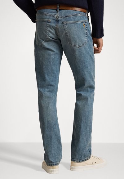Lyseblå denimjeans med rette ben, baklommer og subtile slitasjer. Brukt sammen med en mørk genser og beige sneakers.
