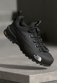 Black hiking shoe with a textured upper, lacing system, and prominent logo. Features a rugged sole with Vibram branding for traction.