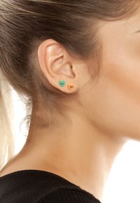 Farbenfrohe herzförmige Ohrringe in Grün und Orange, mit dem Text "xox" und "HI." Das Material scheint glatt mit einem glänzenden Finish zu sein.