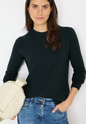 Maglione a coste verde scuro con colletto rotondo, abbinato a jeans in denim azzurro chiaro e una borsa a tracolla crema.