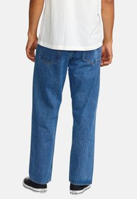 Afslappede blå denim jeans med et klassisk fem-lomme design, lige ben og subtil falmning; båret med en hvid T-shirt og sorte sneakers.