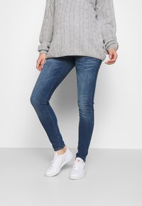 Jeans skinny desbotados em azul, feitos de denim, combinados com um suéter de malha leve em cinza claro e ténis brancos. Apresenta um corte slim e perna afunilada.