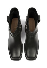 Botas de cuero negro hasta el tobillo con puntera cuadrada, hebillas laterales y un acabado suave. El interior cuenta con una plantilla marrón con el logo de la marca.
