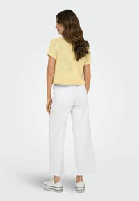 Top giallo corto a maglia con maniche corte, abbinato a pantaloni bianchi a gamba larga. Design semplice, texture leggera, completato con sneakers.